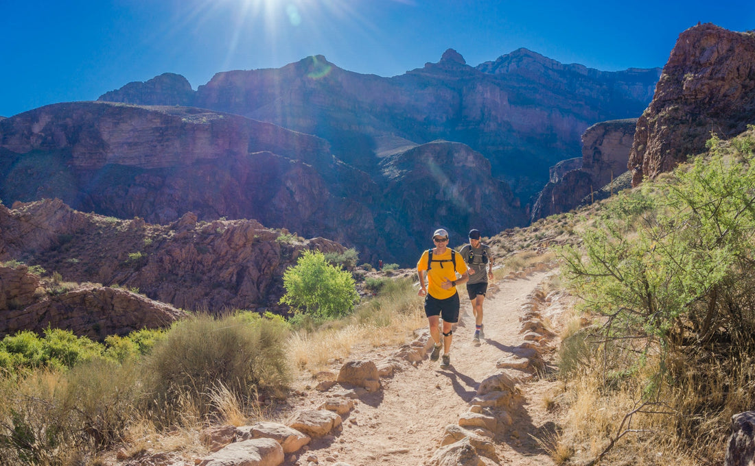 Two trail runners on a rocky path in the Grand Canyon landscape