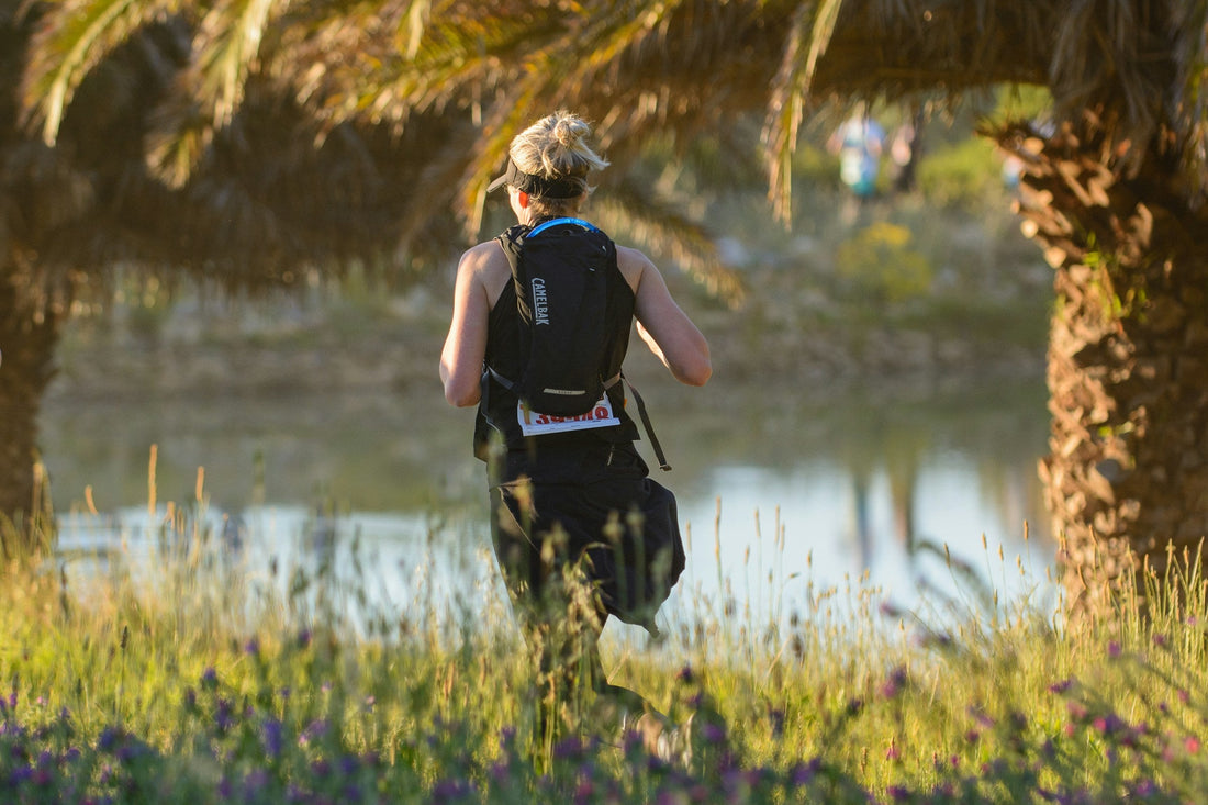 Woman wearing a hydration pack running a trail race beside a pond