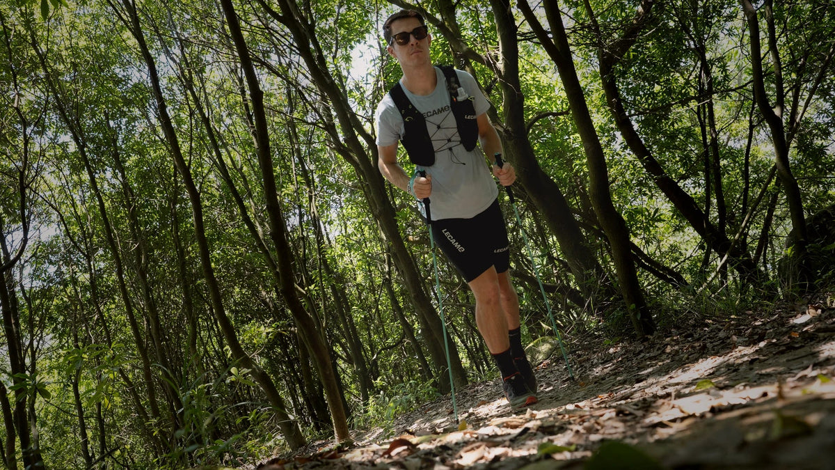LECAMO trail runner climbing through forest with hydration vest and trekking poles