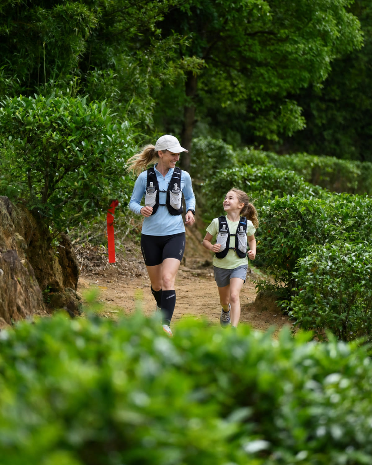 Mother and daughter running together on a green trail